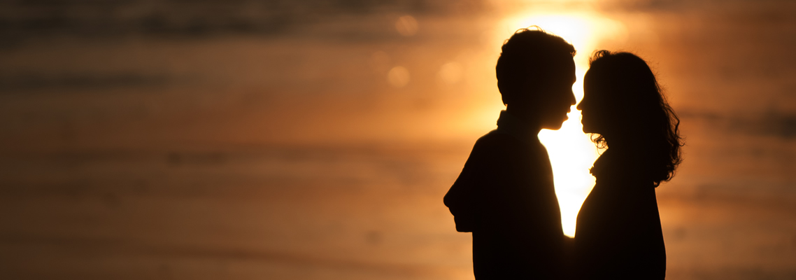 Zwei junge Menschen möchten sich küssen. Im Hintergrund scheint der Sonnenuntergang