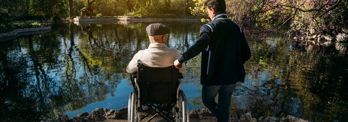 Ein alter Mann auf einem Rollstuhl und ein Kind vor einem kleinen See.